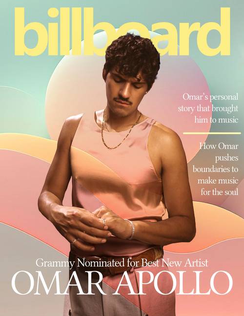 Magazine cover with a seated man in a salmon-colored tank top, pastel curved background shapes and large yellow Billboard lettering.