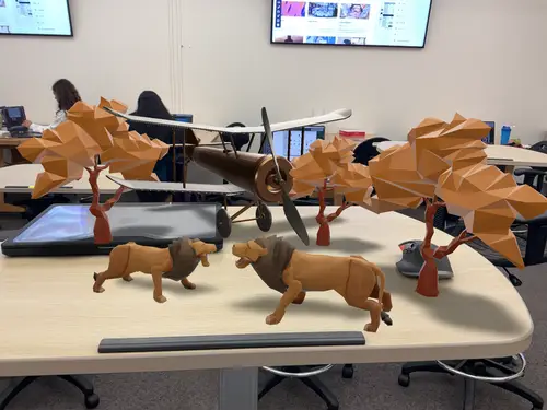 Classroom tabletop scene with two lion figures, orange faceted trees and a propeller aircraft model.