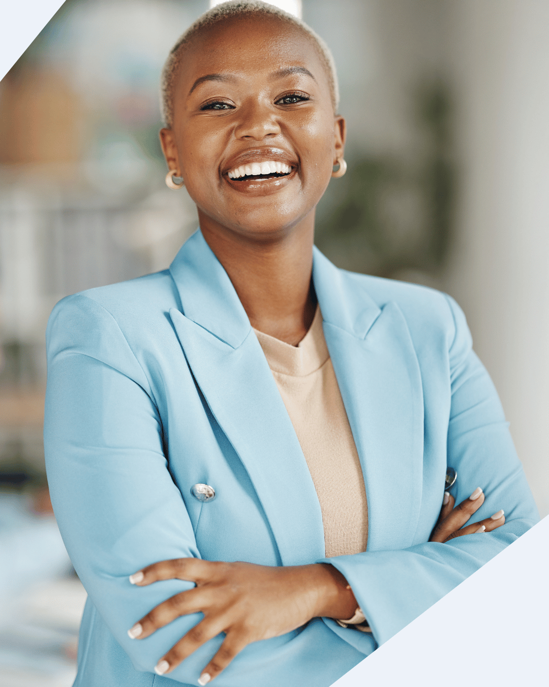Smiling and confident woman looks directly at camera. She wears a light blue blazer over a tan sweater.
