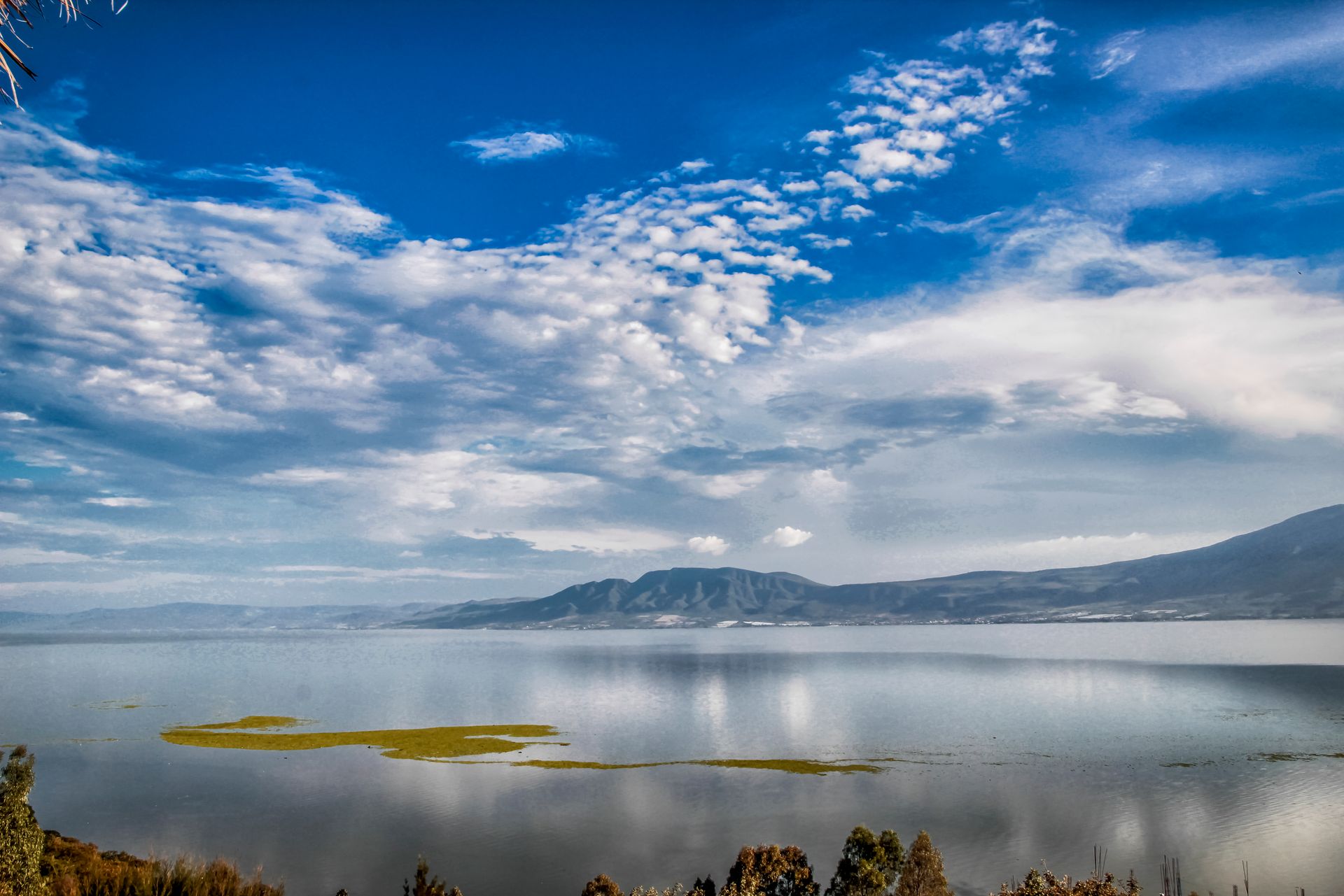 Scenic view of Lake Chapala under a vast cloudy sky with distant mountain silhouettes