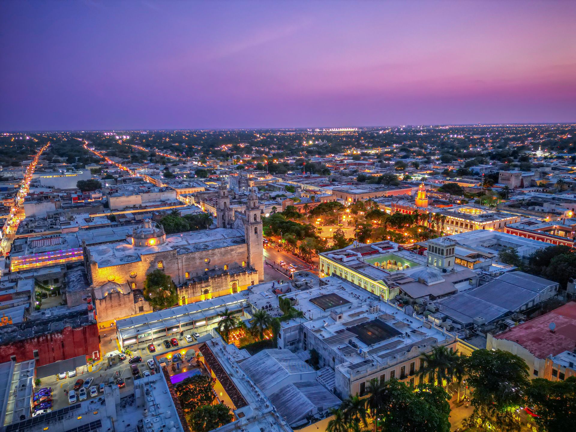 Elevated twilight view of the Mérida Cathedral and historic city center illuminated under a purple dusk sky