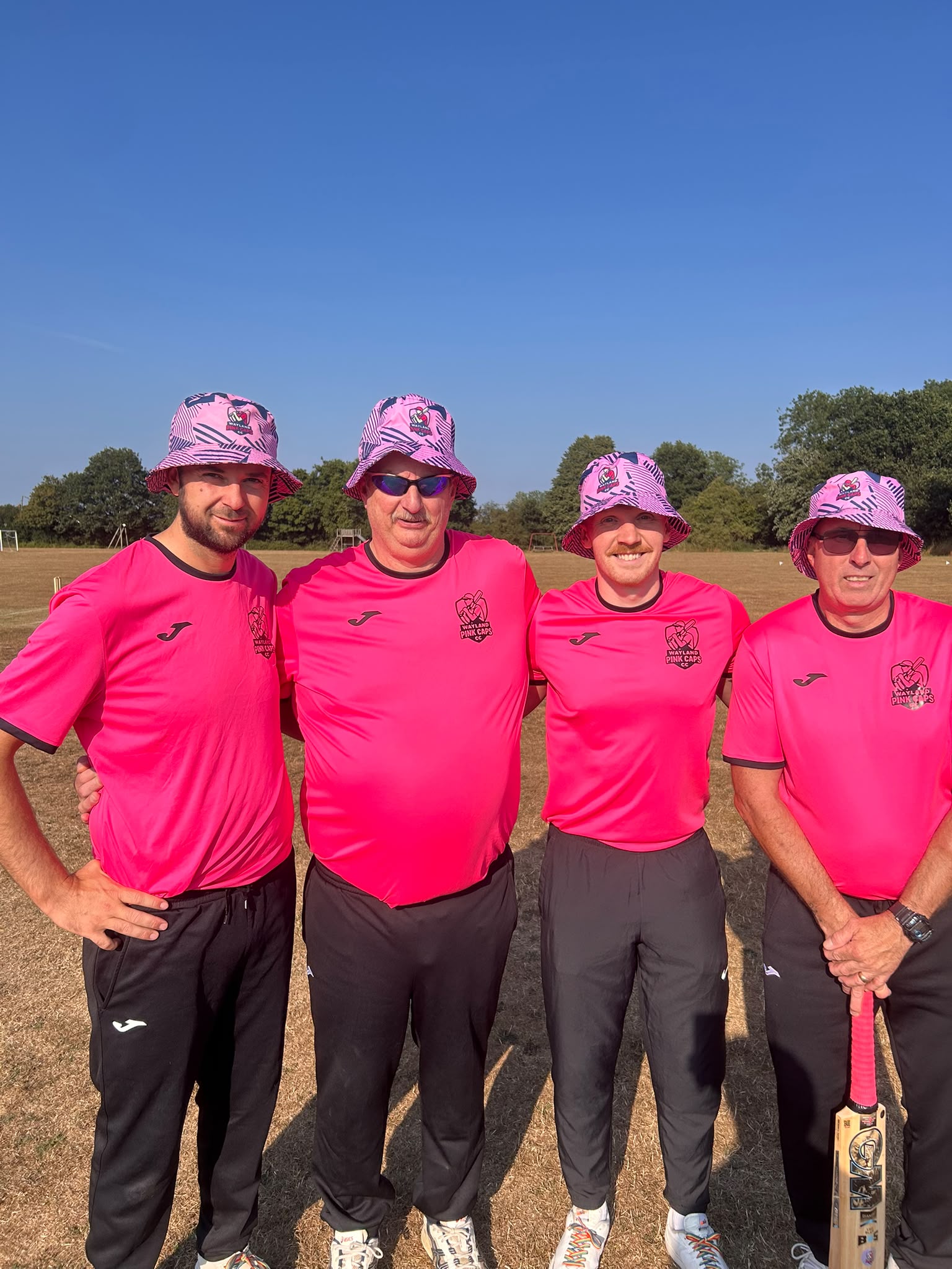 Four Wayland Pink Caps team members wearing matching pink shirts and custom pink bucket hats