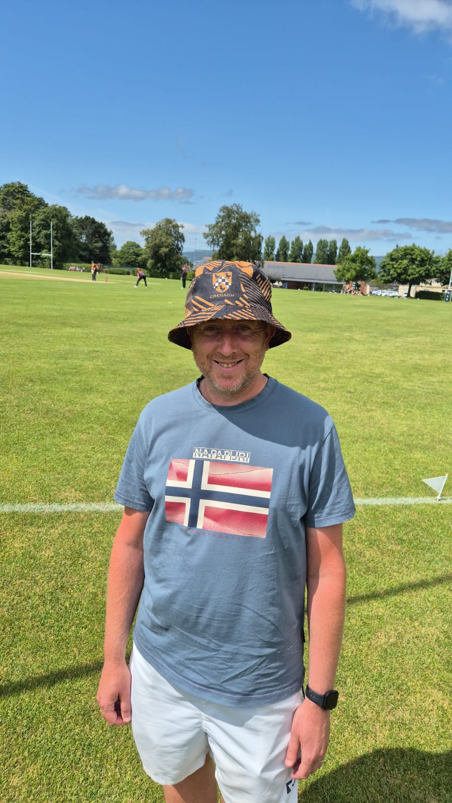 Smiling cricketer wearing Norway flag t-shirt and custom orange and navy Cregagh bucket hat
