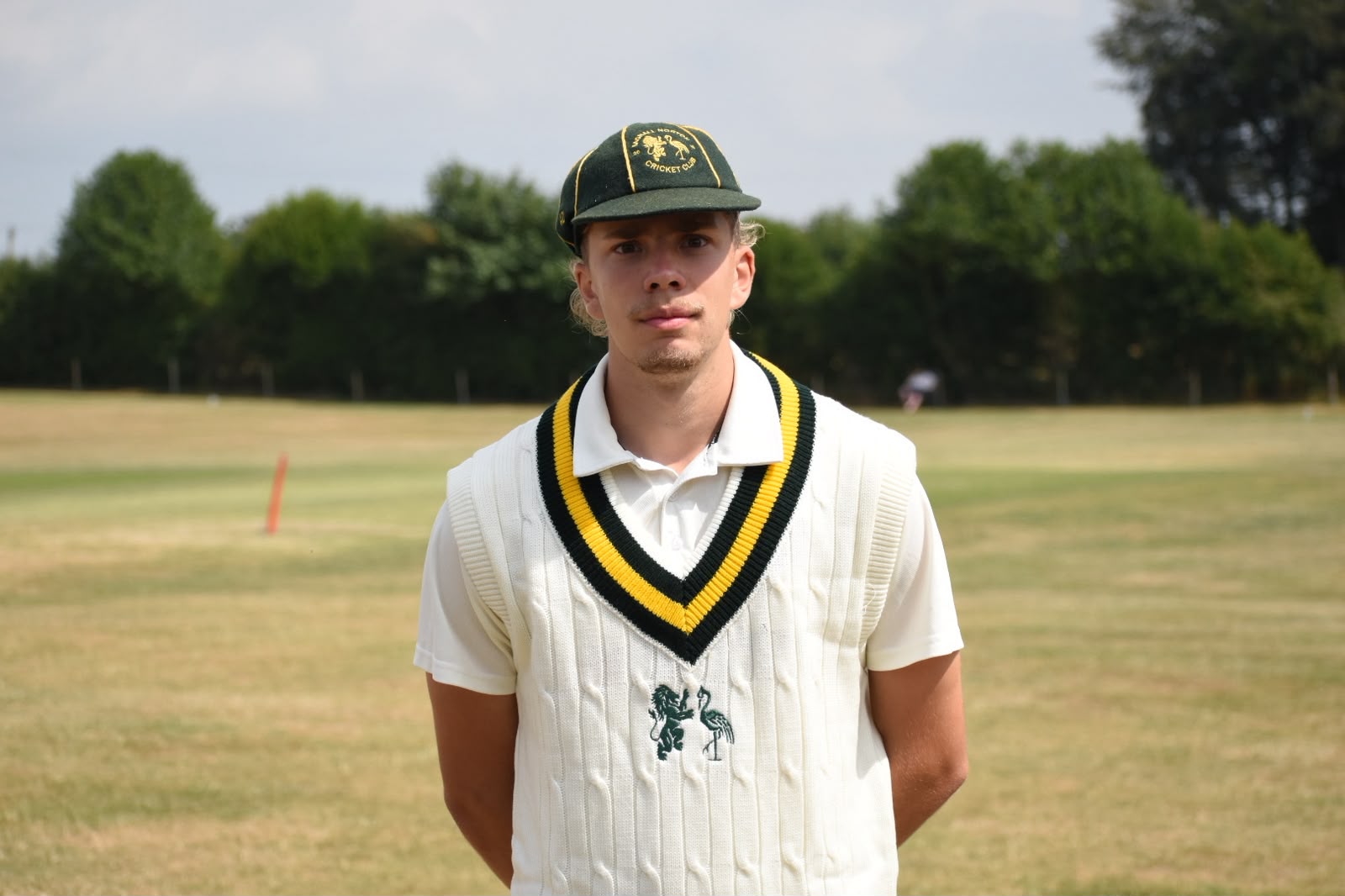 Young cricketer posing in white cricket kit wearing custom green and gold Bredon Cricket Club snapback cap