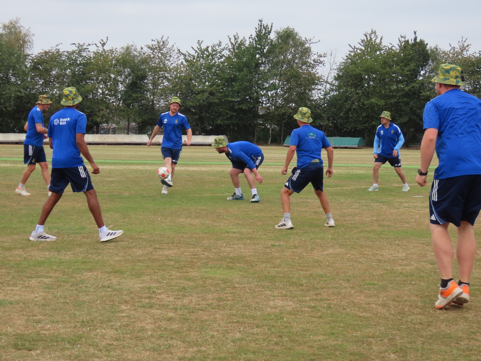 Cricket team warm-up in blue kits with custom yellow and green Cobra bucket hats