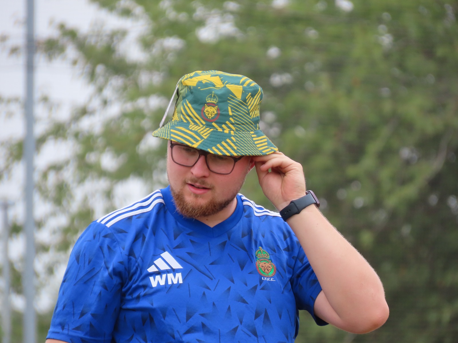 Close-up of cricketer wearing custom yellow and green Cobra bucket hat with team crest