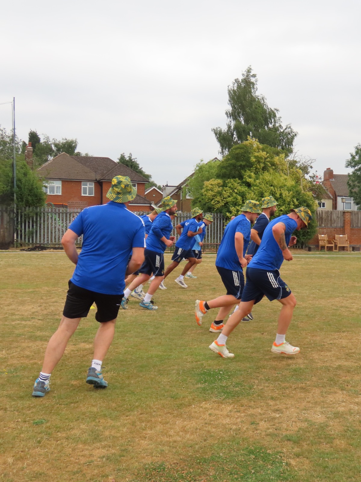 Cricket team training in blue kits wearing yellow and green patterned Cobra bucket hats
