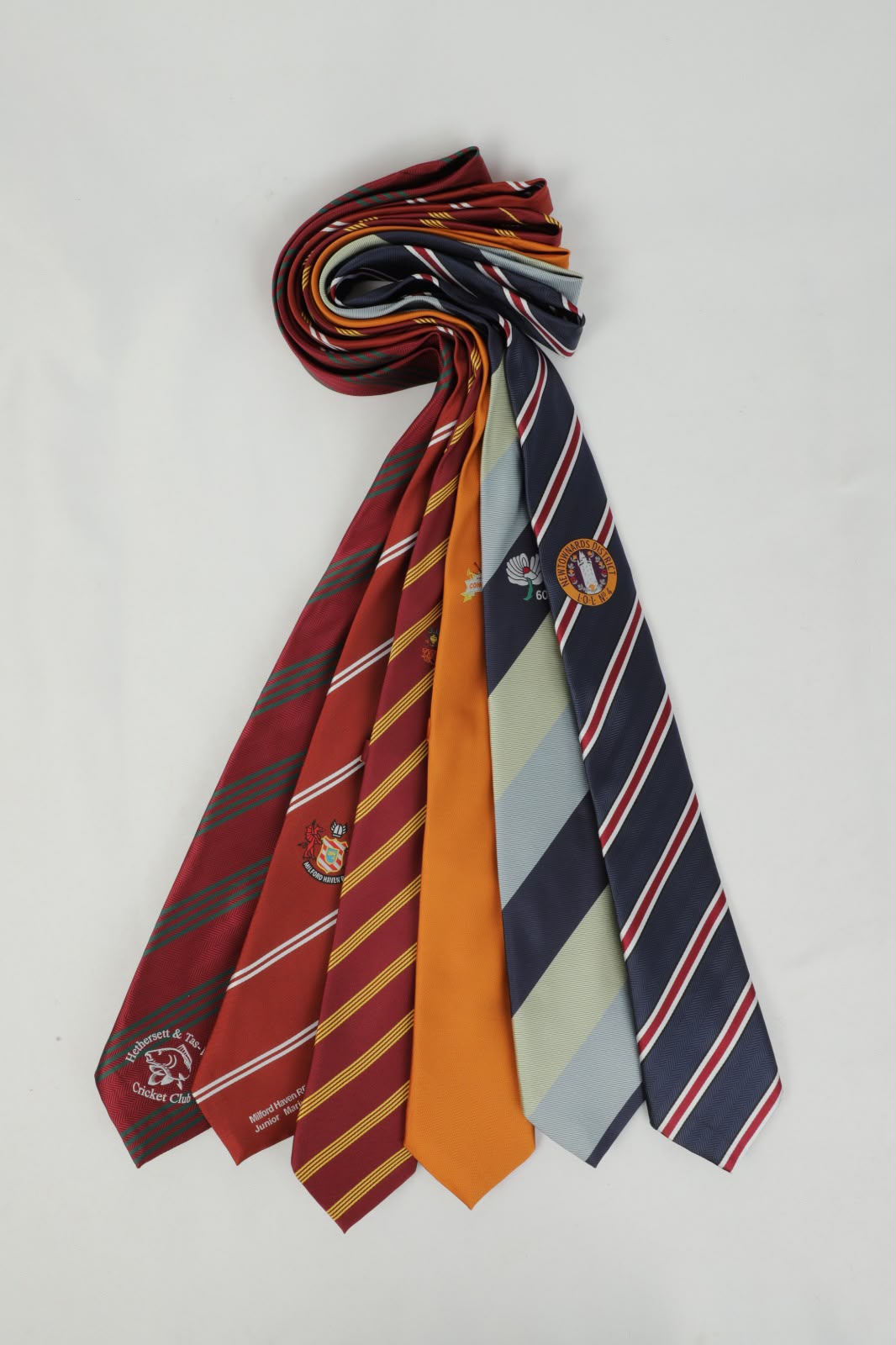 Colourful custom club ties with crests laid out on a white surface