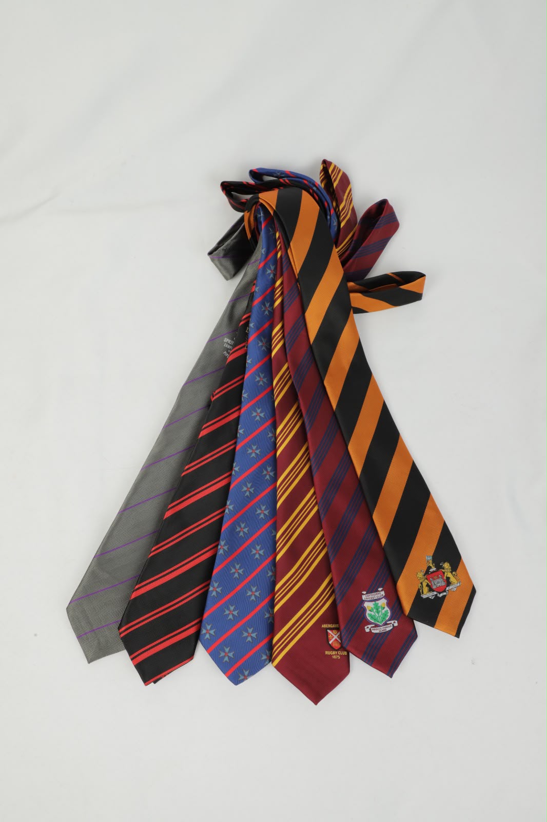 Fan of custom club ties laid out in a row — multiple colours and patterns