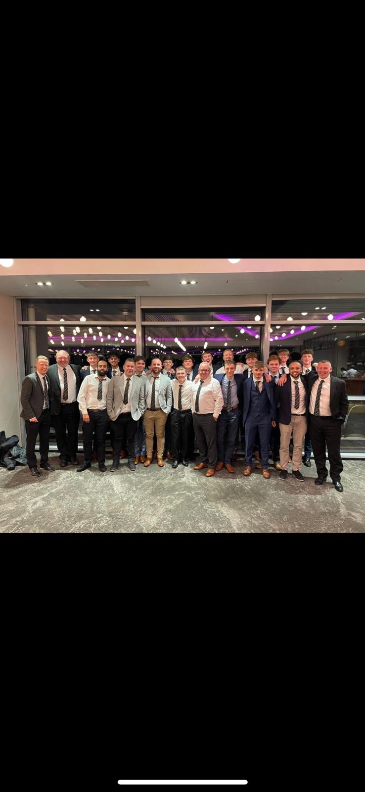Large group of members in formal suits wearing matching club ties at a black-tie event