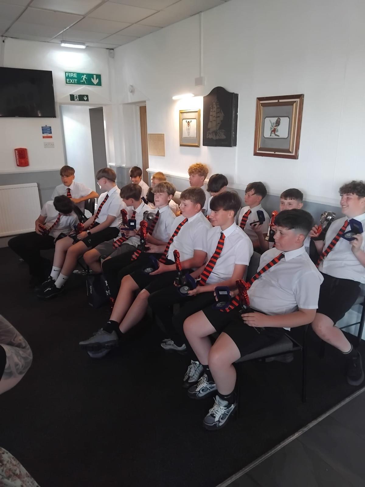 Row of school-age boys in white shirts and dark shorts wearing red and black striped club ties at an awards night