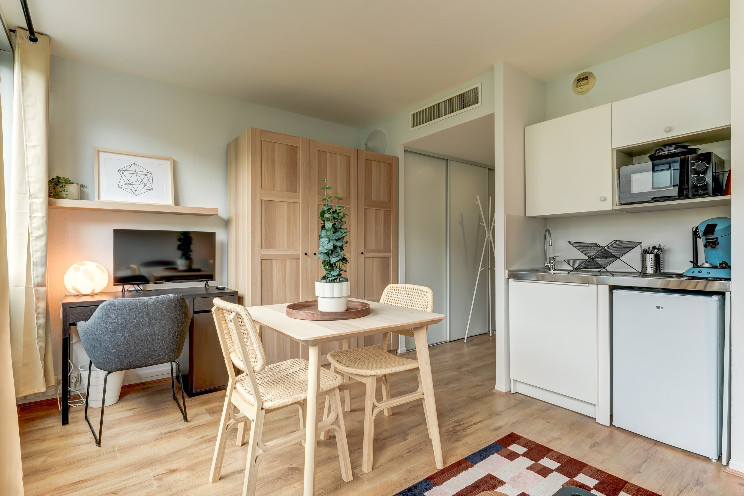 Studio rénové à Villeurbanne, avenue Salengro : cuisine équipée ouverte sur coin salon avec mobilier soigné, parquet clair et télévision