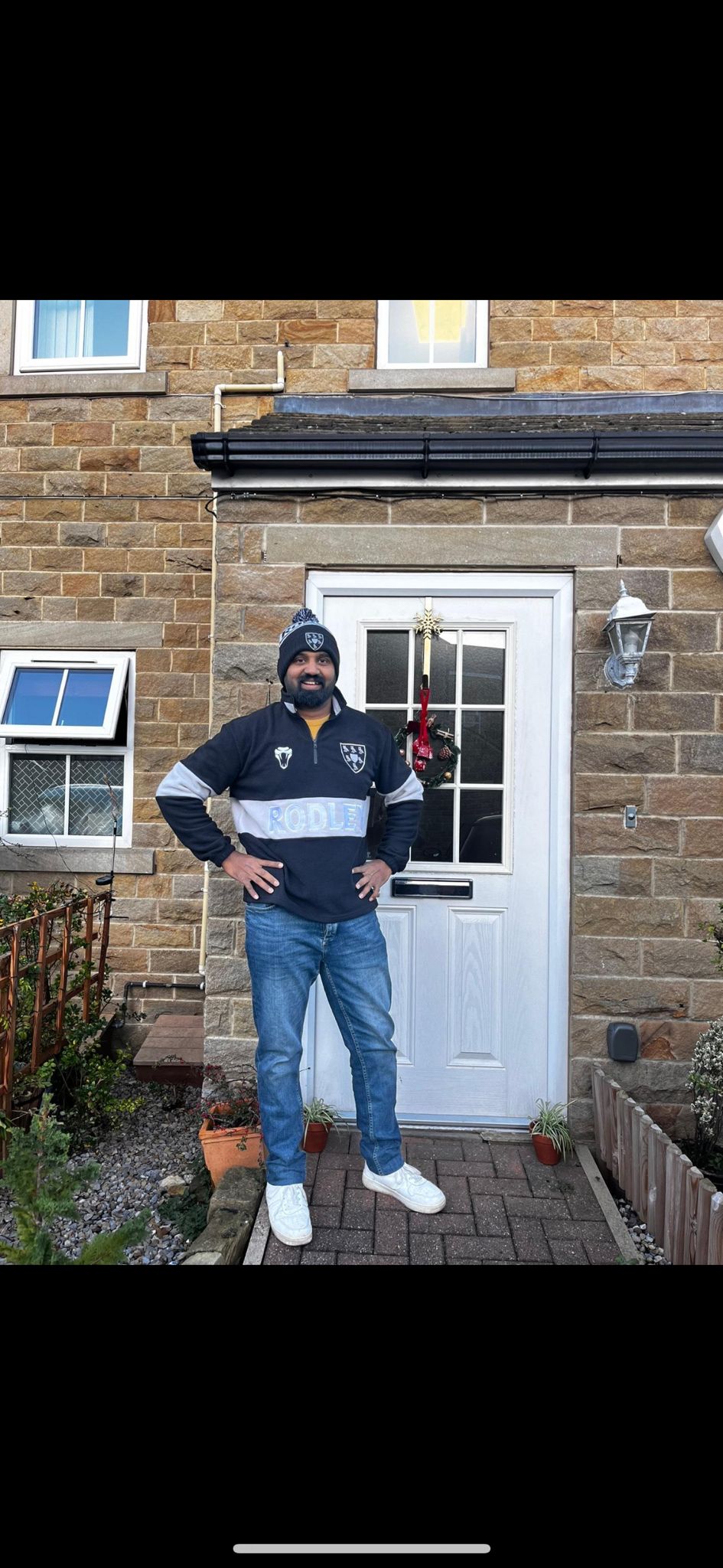 A Rodley CC supporter wearing a navy and white custom bobble hat at his front door