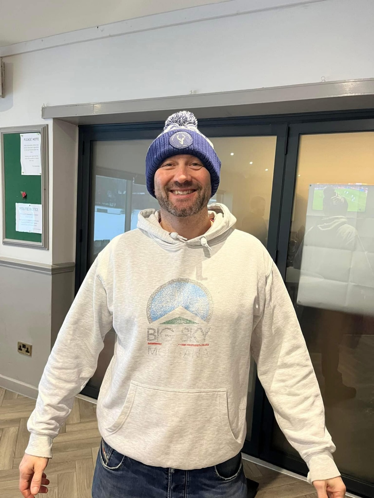 A Bacup CC supporter wearing a purple and white custom bobble hat indoors