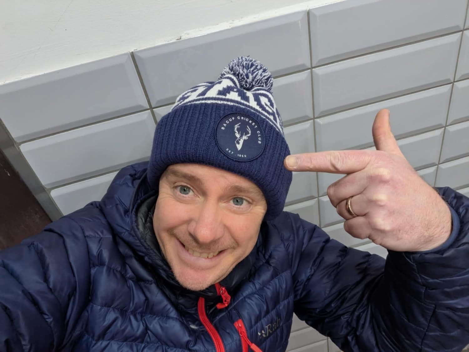 A Bacup CC supporter wearing a navy and white custom bobble hat indoors