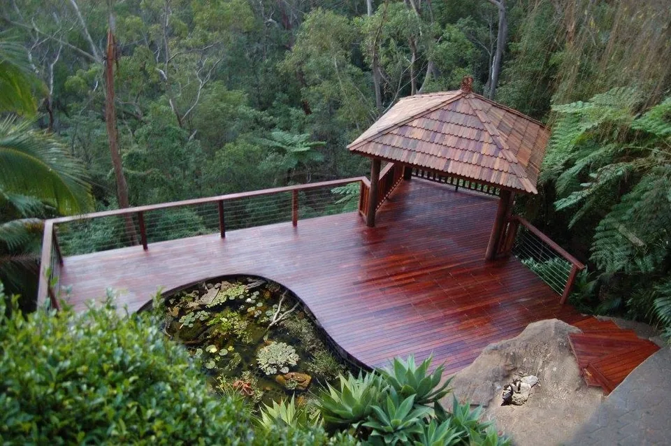 The finished timber gazebo and deck from the top of the page, with a shingled roof, set among gum trees above a pond.